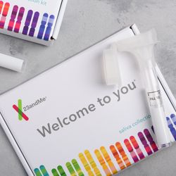 23andMe personal genetic test saliva collection kit, with tube and box on table overhead view.