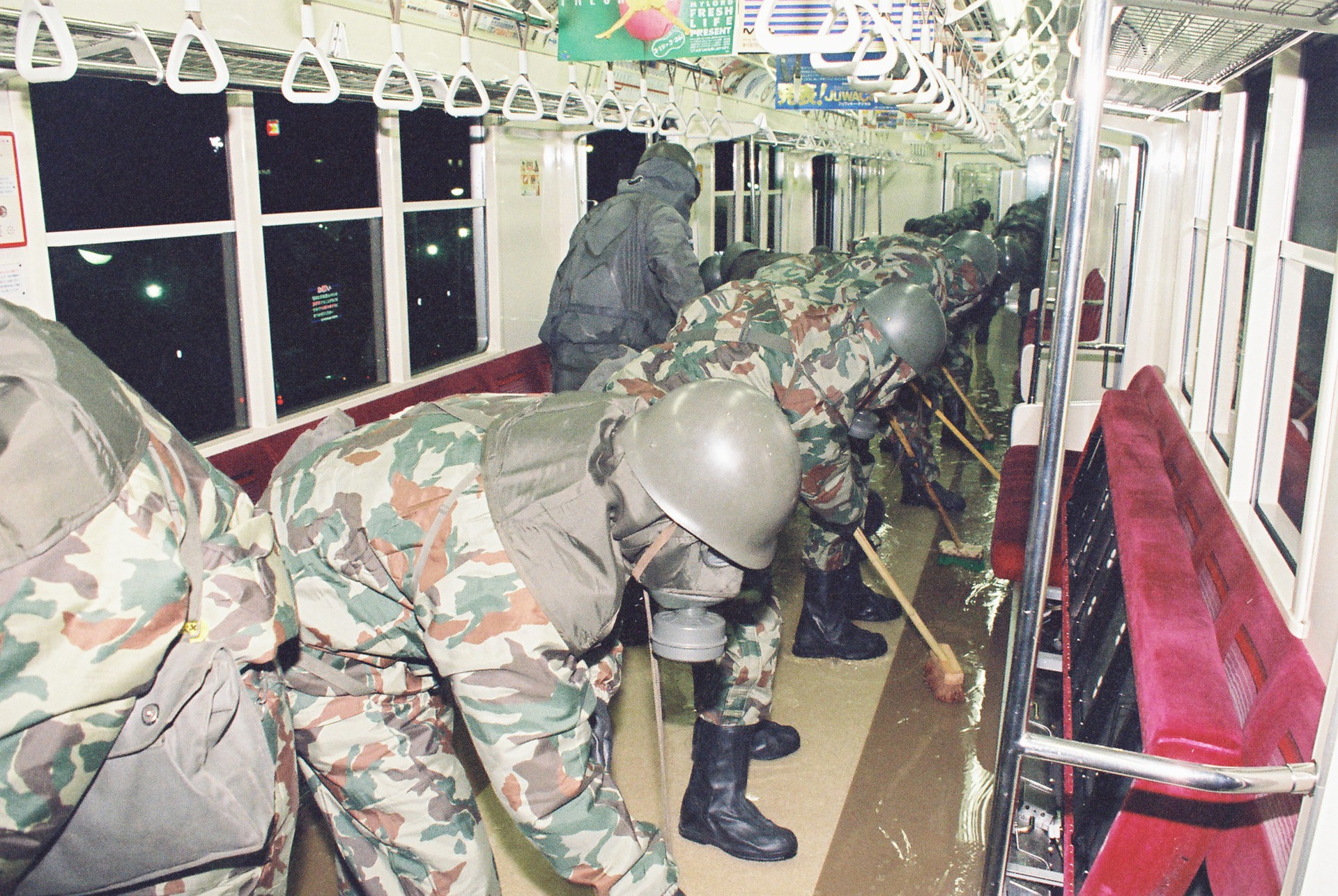 A line of military officers are scrubbing the floor of a train in the Tokyo underground. The men are wearing camouflaged suits, gas masks and helmets. They are all leaning over brooms and rubbing a liquid that covers the floor of the carriage. A line of military officers are scrubbing the floor of a train in the Tokyo underground. The men are wearing camouflaged suits, gas masks and helmets. They are all leaning over brooms and rubbing a liquid that covers the floor of the carriage.