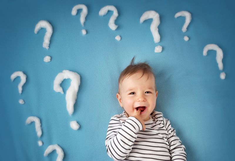 baby lying on a blue mat surrounded by question marks made of cotton wool