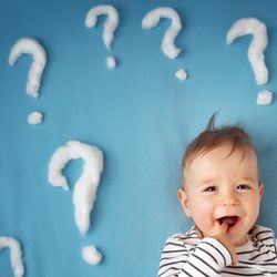 baby lying on a blue mat surrounded by question marks made of cotton wool