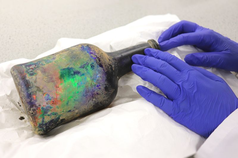 A scientist with rubber gloves touches an old bottle  made between 1790 and 1840.