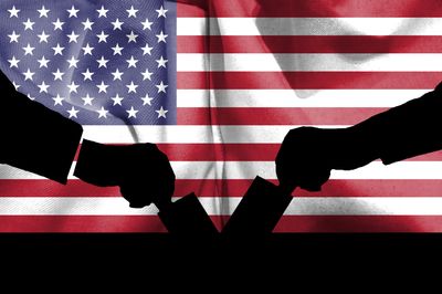 silhouettes of two hands putting ballot papers in a ballot box with the backdrop of the US flag