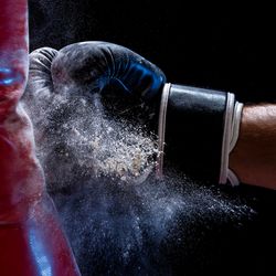 Close-up hand of boxer at the moment of impact on punching bag over black background