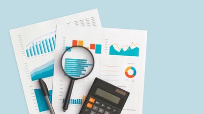 top-down view of business graphs and charts on table, with a magnifying glass, calculator, and pen laying on top