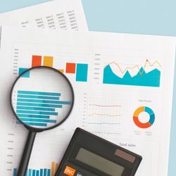 top-down view of business graphs and charts on table, with a magnifying glass, calculator, and pen laying on top