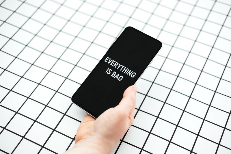 A photo of a person's hand holding a smart phone with the words "Everything is bad" on the screen. The and hand is set against a black and white grid background. 