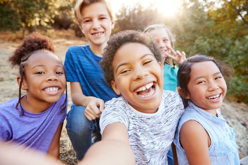 group of young kids in a selfie taken outdoors; they are of a mixture of genders and racial backgrounds