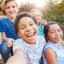 group of young kids in a selfie taken outdoors; they are of a mixture of genders and racial backgrounds