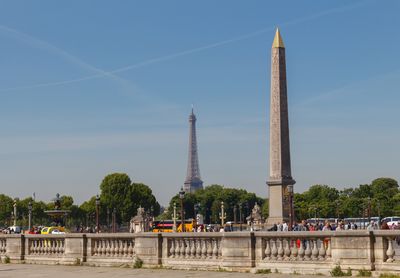 A photo showing the Luxor obelisk with the Eiffel Tower in the background. The obelisk has its characteristic golden pointed top and you can just make out some of the hieroglyphs on its side. The photo sits within a wider shot that also captures the busy tourists walking up the Place de la Concorde.
