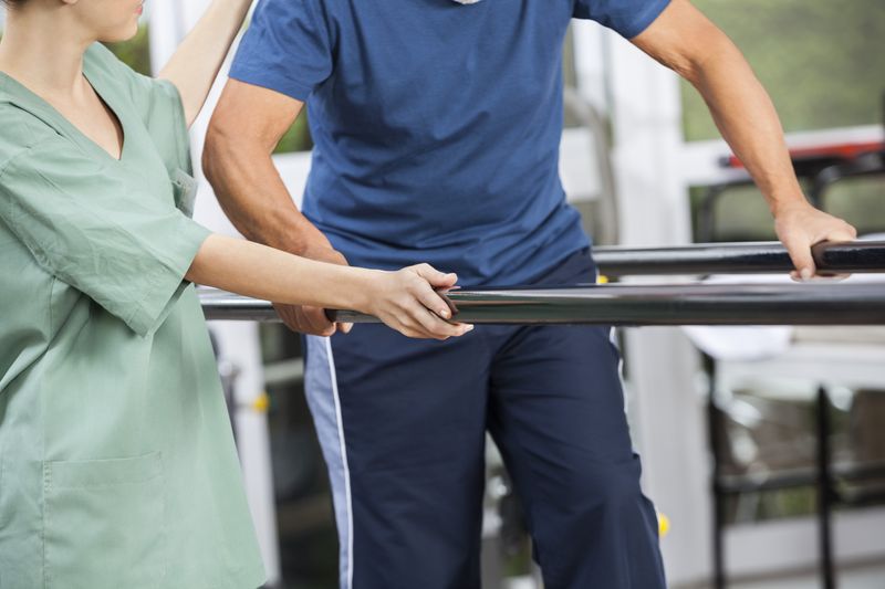 Man learning to walk again with the help of a physiotherapist and parallel bars