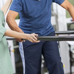 Man learning to walk again with the help of a physiotherapist and parallel bars