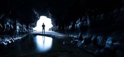 Man standing at the entrance of a dark cave, silhouetted by light