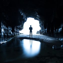 Man standing at the entrance of a dark cave, silhouetted by light