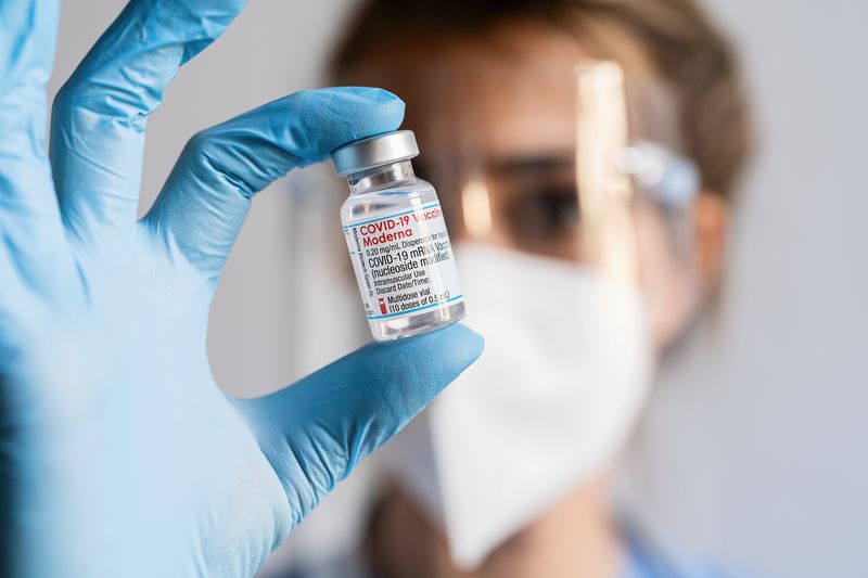 healthcare worker wearing mask, face shield and gloves holding vial of Moderna mRNA COVID vaccine