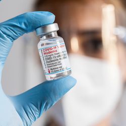 healthcare worker wearing mask, face shield and gloves holding vial of Moderna mRNA COVID vaccine