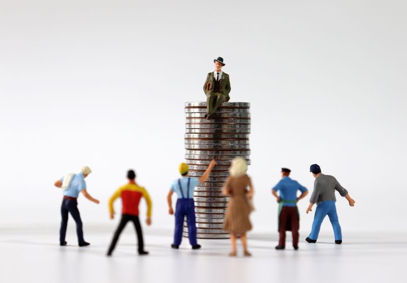 small figurines of people facing a figurine of a man in a suite and hat sitting high up on a pile of coins