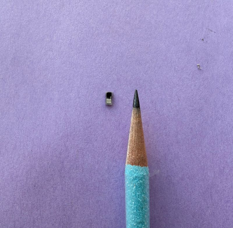 tiny black rectangle next to a blue graphite pencil; the rectangle is smaller than the tip of the pencil. They're on a purple background
