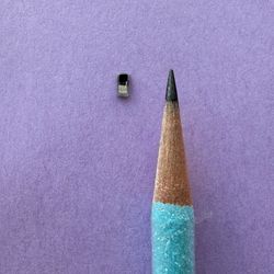 tiny black rectangle next to a blue graphite pencil; the rectangle is smaller than the tip of the pencil. They're on a purple background