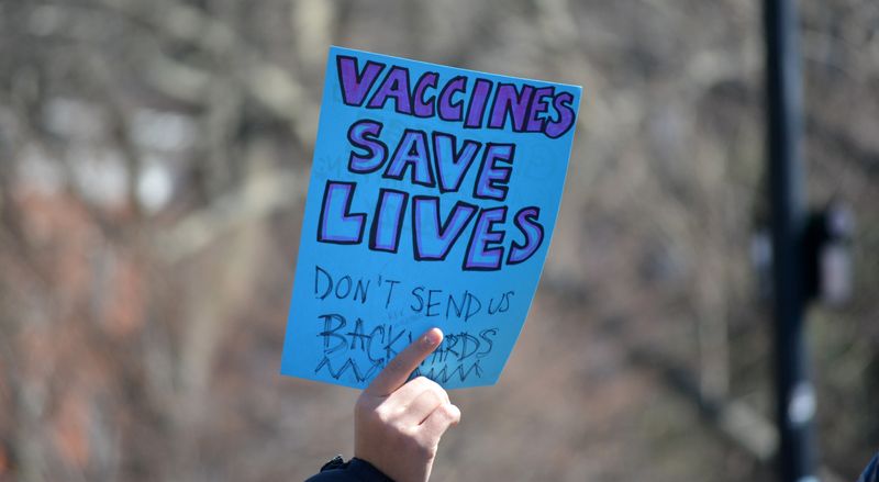 hand holding blue sign that reads "vaccines save lives, don't send us backwards." Photographed March 7 during the Stand up for Science rally against DOGE cuts to scientific research in Washington Square Park in Manhattan.