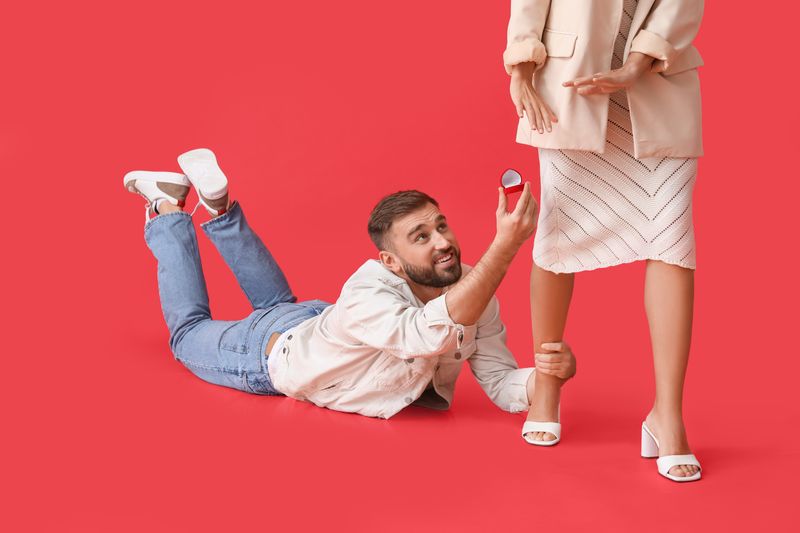 Young woman rejecting marriage proposal, the man is laying on the floor holding onto her leg