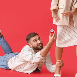 Young woman rejecting marriage proposal, the man is laying on the floor holding onto her leg
