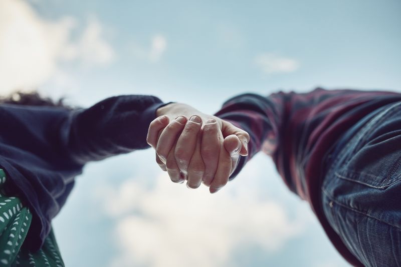Couple holding hands shot from below with the sky in the background