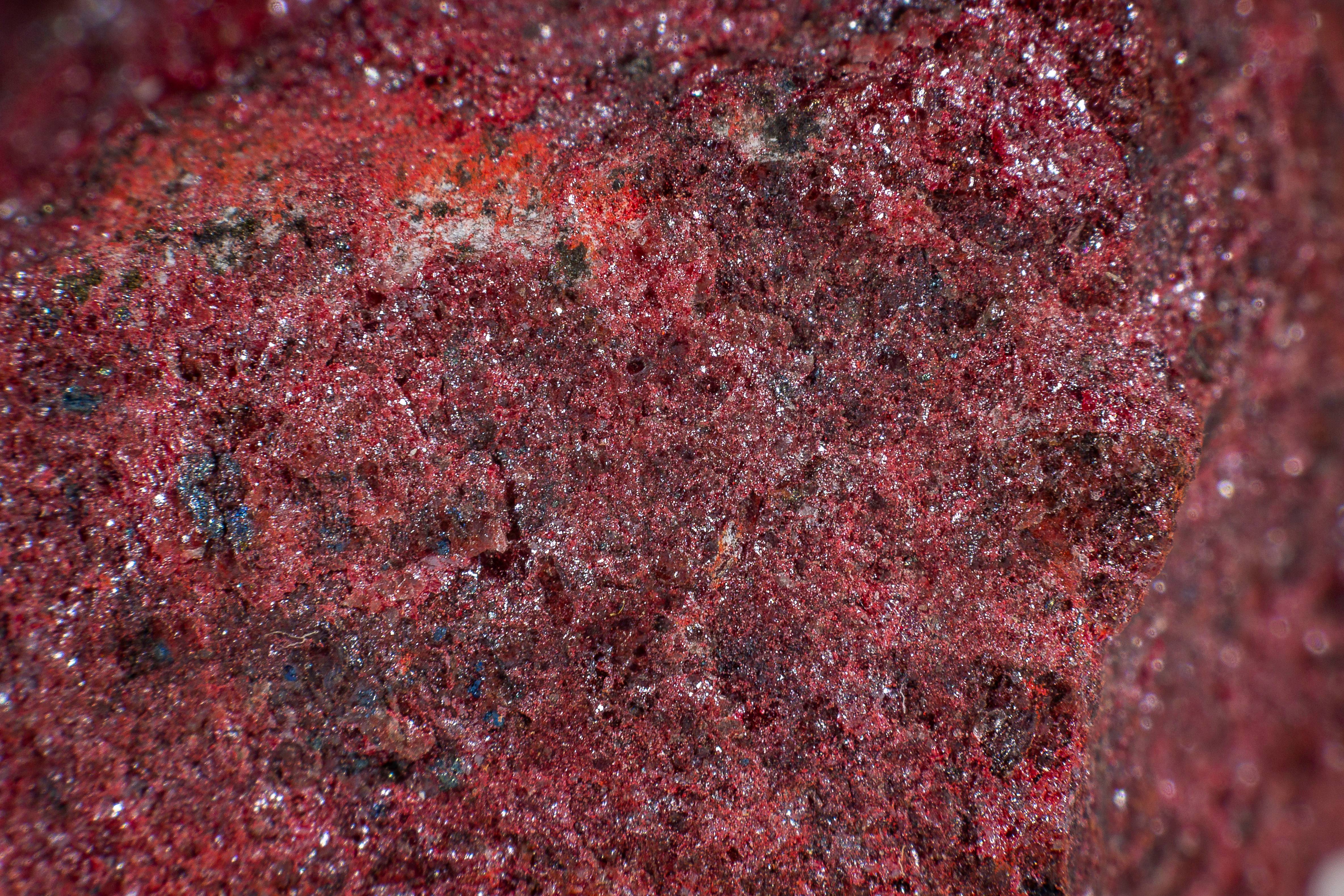 A close up of cinnabar mineral stone. The surface is a deep read with a rough crystalline texture. Some patches of crystal are bigger than others, giving it a darker red look. A close up of cinnabar mineral stone. The surface is a deep read with a rough crystalline texture. Some patches of crystal are bigger than others, giving it a darker red look.