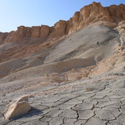Male tourist in a hiking trail descending from a top of the Mount Zin or Har Zin in the Har Hahar nature reserve in Negev Desert. Unique landscape of the mount. Dried up cracked soil in the foreground