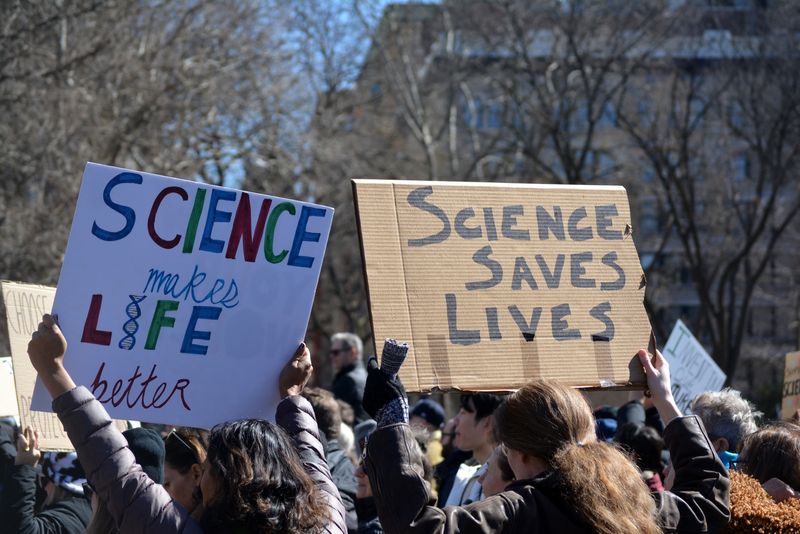 two placards being held up at the Stand up for Science rally in Washington Square Park, Manhattan, on March 7 2025. One reads "Science makes life better" and the other reads "Science saves lives"