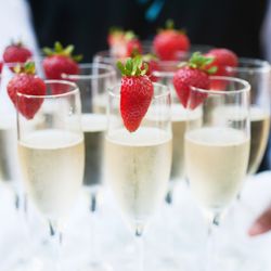 close up of tray being carried by a waiter, holding several flutes of champagne each with a strawberry wedged onto the top of the glass