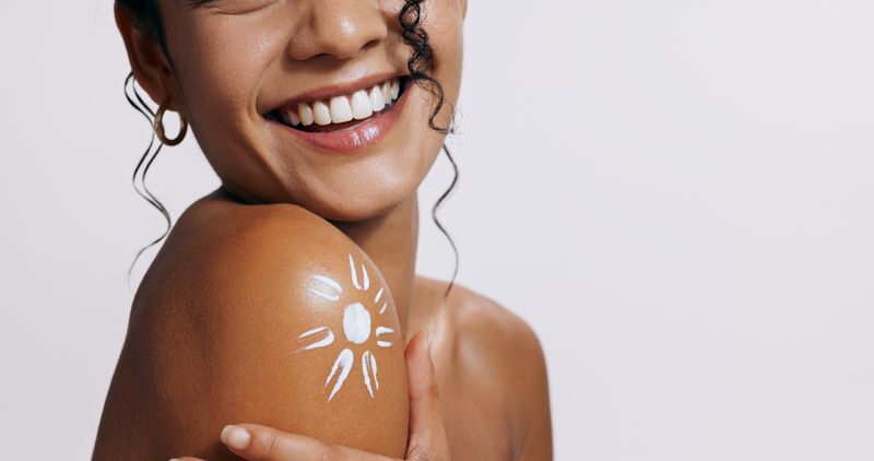 a woman showing a tanned shoulder with a sun drawn in sunscreen on it