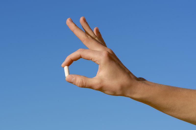 A hand holding a white pil on a blue background