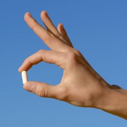 A hand holding a white pil on a blue background