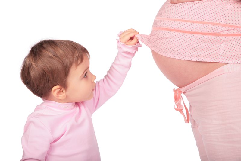 Toddler in pink shirt lifting up pregnant person's pink shirt to reveal belly