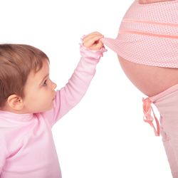 Toddler in pink shirt lifting up pregnant person's pink shirt to reveal belly