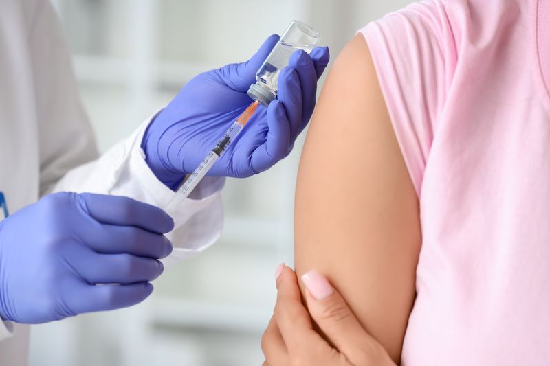 close up of doctor's hands as they draw up a vaccine in a syringe next to the patient's arm, with sleeve rolled up ready to get the shot