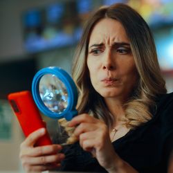 Woman looking at phone through magnifying glass looking perplexed