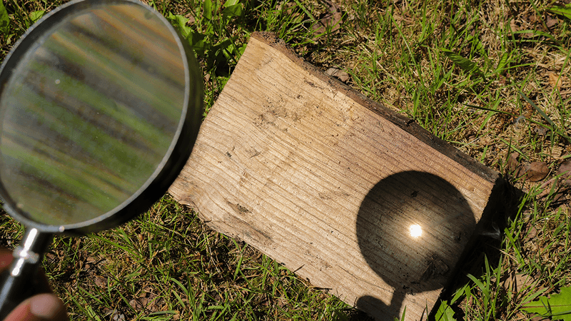 Magnifying glass focusing light onto a piece of wood.