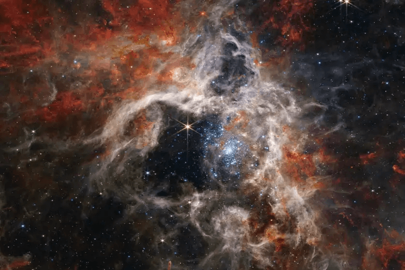 wispy clouds of different colours open around a middle central region where many bright stars are clearing our the gas