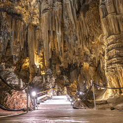 Huge cavern filled with stalactites and stalagmites with a lit pathway with roped edges.