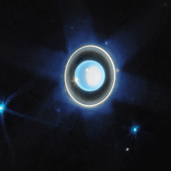 The planet Uranus is on a black background just left of centre. Just below the planet at the 7 o’clock position is a faint blue point labeled Puck. Brighter blue points at 8 o’clock, 5 o’clock, and 3 o’clock are labeled Ariel, Miranda, and Umbriel, respectively.